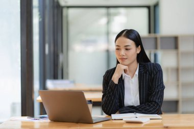 Asyalı iş kadını, grafiği gösteren bir raporu kalem, dizüstü bilgisayar ve hesap makinesiyle analiz ediyor. İş istasyonu muhasebecisinde tele pazarlama konsepti, ekommerce, ücretsiz online pazarlama.