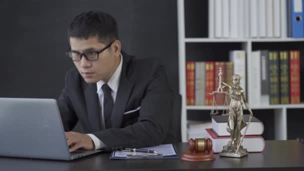 ハンマーノートパソコンで働くアジアの男性弁護士法律事務所で正義の女神 オンラインコンサルティングの概念 — ストック動画