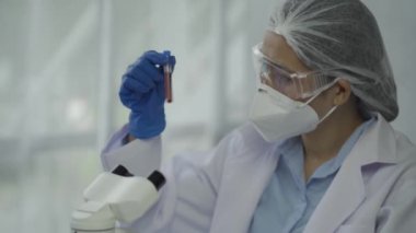 Laboratuvarda kimya deneyleri yapan kadın bir bilim adamı. Şapkalı ve maskeli güzel bir kadın doktor, kırmızı ve yeşil sıvı içeren cam bir şişeye test tüpü yerleştiriyor..