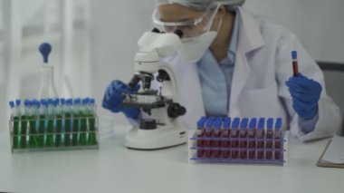 Laboratuvarda kimya deneyleri yapan kadın bir bilim adamı. Şapkalı ve maskeli güzel bir kadın doktor, kırmızı ve yeşil sıvı içeren cam bir şişeye test tüpü yerleştiriyor..