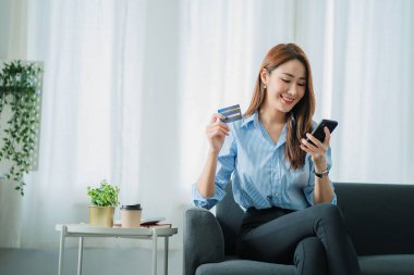 Güzel bir Asyalı kadın evdeki kredi kartıyla evde online alışveriş yapıyor. Bir kadın akıllı telefon kullanıyor ve online işlem yapıyor. çevrimiçi alışveriş kavramı