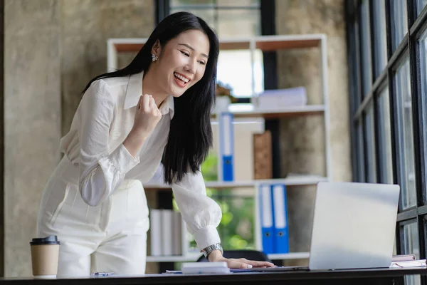 Young Asian business woman excited about successful business in front of online finance concept laptop.