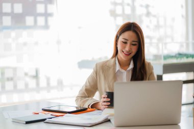 Modern ofiste dizüstü bilgisayarı olan mutlu gülümseyen Asyalı iş kadını online muhasebe kavramını finanse ediyor.