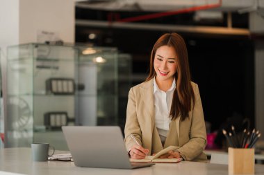 Modern ofiste dizüstü bilgisayarı olan mutlu gülümseyen Asyalı iş kadını online muhasebe kavramını finanse ediyor.