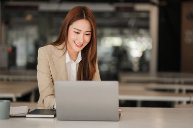 Modern ofiste dizüstü bilgisayarı olan mutlu gülümseyen Asyalı iş kadını online muhasebe kavramını finanse ediyor.