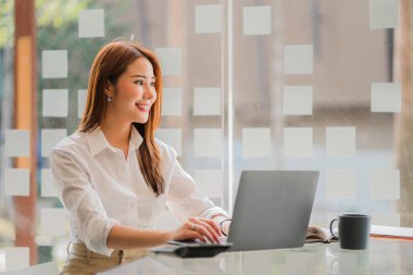 Modern ofiste dizüstü bilgisayarı olan mutlu gülümseyen Asyalı iş kadını online muhasebe kavramını finanse ediyor.