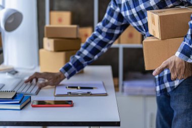 Çevrimiçi iş fikri, genç girişimci, evde dizüstü bilgisayarla ve akıllı telefonla çalışıyor, siparişleri alıyor ve paketleri teslim ediyor..