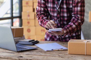 Çevrimiçi iş fikri, genç girişimci, evde dizüstü bilgisayarla ve akıllı telefonla çalışıyor, siparişleri alıyor ve paketleri teslim ediyor..