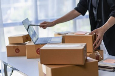 Çevrimiçi iş fikri, genç girişimci, evde dizüstü bilgisayarla ve akıllı telefonla çalışıyor, siparişleri alıyor ve paketleri teslim ediyor..
