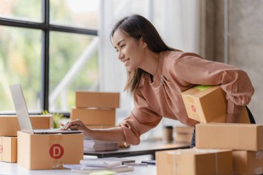 Asyalı bir kadın küçük bağımsız bir işe başlıyor. Paket kutuları ve dizüstü bilgisayarlarla oturuyor. Evindeki oturma odasındaki ahşap masada üç akıllı telefon..