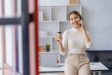 Akıllı telefondan konuşan Asyalı bir kadın, evden çalışıyor, dijital telefon teknolojisi yaşam tarzı evde çalışıyor ve dizüstü bilgisayar finansal konseptiyle çalışıyor.