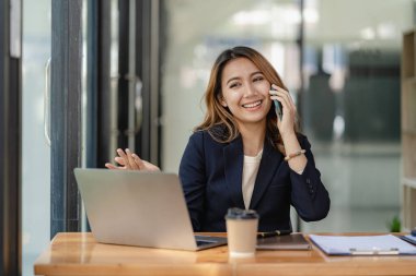 Akıllı telefondan konuşan Asyalı bir kadın, evden çalışıyor, dijital telefon teknolojisi yaşam tarzı evde çalışıyor ve dizüstü bilgisayar finansal konseptiyle çalışıyor.