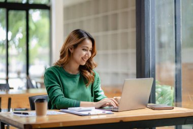 Asyalı bir kadın muhasebeci elinde dizüstü bilgisayarla masada oturuyor ve başarılı yatırım planlaması sonuçlarını gösteren bir mali grafik hesaplıyor..