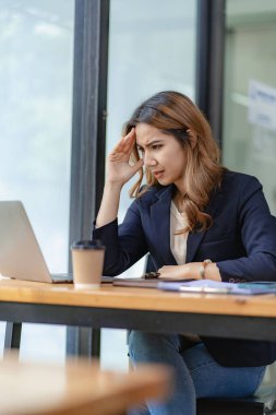 Asyalı bir kadın muhasebeci elinde dizüstü bilgisayarla masada oturuyor ve başarılı yatırım planlaması sonuçlarını gösteren bir mali grafik hesaplıyor..
