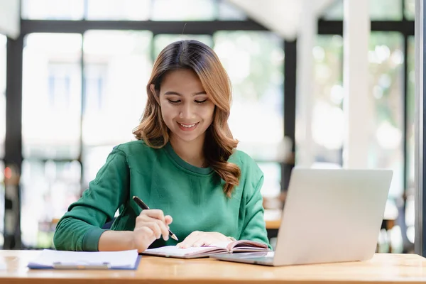 stock image An Asian female accountant sits at a desk with a laptop working and calculates a financial graph showing results about successful investment planning.