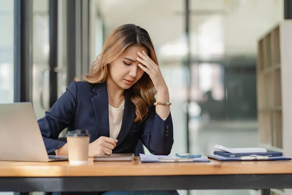 stock image An Asian female accountant sits at a desk with a laptop working and calculates a financial graph showing results about successful investment planning.