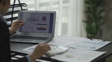 Elinde kağıt, grafik kağıdı ve dizüstü bilgisayar kullanan serbest çalışan bir kadın, Asyalı iş kadını kendi şirketinin bütçe analizinde çalışıyor..