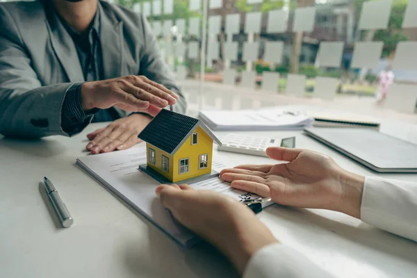 real estate Sales representatives talk about loans and interest rates, offer home purchase contracts to buy a house or apartment, and give a house key to a customer in the office.