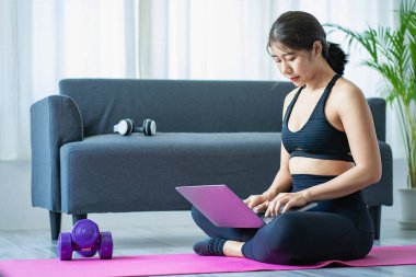 Halter kullanarak egzersiz yapan Asyalı bir kadın yoga yapan, meditasyon yapan, evde gezen spor kıyafetleri giyen, vücut fotoğrafı çeken ve meditasyon yapan güzel bir kadın. sağlıklı yaşam tarzı