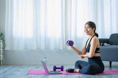 Halter kullanarak egzersiz yapan Asyalı bir kadın yoga yapan, meditasyon yapan, evde gezen spor kıyafetleri giyen, vücut fotoğrafı çeken ve meditasyon yapan güzel bir kadın. sağlıklı yaşam tarzı