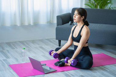 Halter kullanarak egzersiz yapan Asyalı bir kadın yoga yapan, meditasyon yapan, evde gezen spor kıyafetleri giyen, vücut fotoğrafı çeken ve meditasyon yapan güzel bir kadın. sağlıklı yaşam tarzı