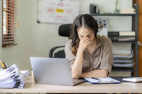 Stock image Asian businesswoman headache during work analyzing financial graphs with laptop at her desk stressed woman Headache during overtime at home office