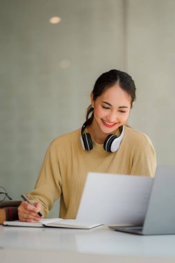 Asyalı liseli kız, internetten bilgisayar kullanarak öğreniyor, kulaklık takıyor, internetten öğreniyor ve uzaktan öğreniyor.