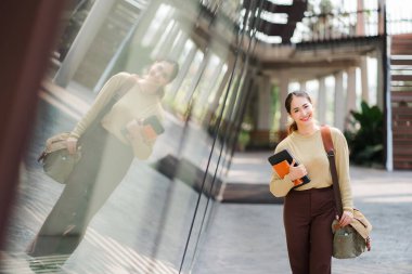 Asyalı kız öğrenci elinde bir tabletle üniversite binasının yanında yürümek için çanta taşıyor. Eğitim kavramı..