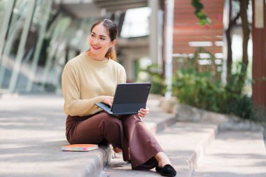Asyalı kız öğrenci elinde tabletle yerde oturuyor ve üniversitede tabletle ders çalışıyor ya da özel okulda teknoloji öğretiyor.