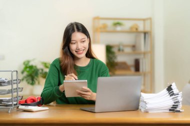 Masandaki dizüstü bilgisayarla pazarlama verilerini planlayan ve analiz eden bir yığın finansal grafik çizelgesi ile çalışan genç Asyalı kadın. Şirket bilgi bürosu