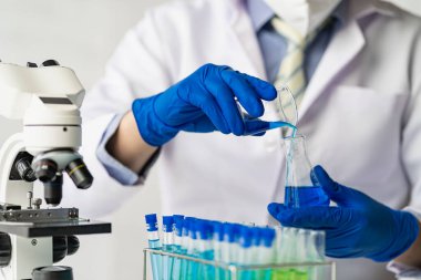 Laboratuvar önlüklü bir bilim adamı ya da doktor, biyokimyasal laboratuvar araştırması yapan cam bir aparatta reaktif mikroskop ve renkli bir sıvı kullanarak test tüpü tutuyor..