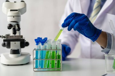Laboratuvar önlüklü bir bilim adamı ya da doktor, biyokimyasal laboratuvar araştırması yapan cam bir aparatta reaktif mikroskop ve renkli bir sıvı kullanarak test tüpü tutuyor..