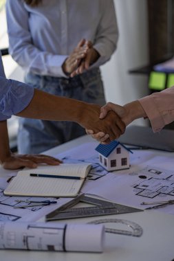 Mimarlar ve mühendisler planlı binalara işaret ediyor ve bir inşaat konsept ofisinde ev projesi tasarımları çizmek için dizüstü bilgisayar kullanıyorlar..