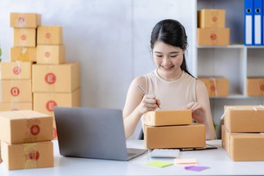 Genç Asyalı kadın internette KOBİ işi için bir kutu ve dizüstü bilgisayar satarak çalışıyor. Paket teslim kavramı.