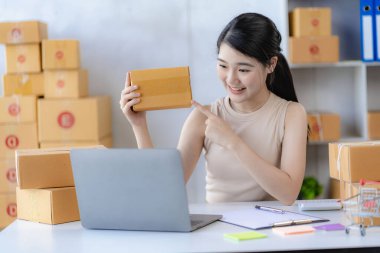 Genç Asyalı kadın internette KOBİ işi için bir kutu ve dizüstü bilgisayar satarak çalışıyor. Paket teslim kavramı.