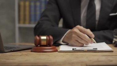 Ofiste çalışan genç erkek avukat iş adamı ya da avukat dizüstü bilgisayar sözleşmesi belgelerini tartışıyor ve yargıcın çekicini masaya koyuyor. 4k video.