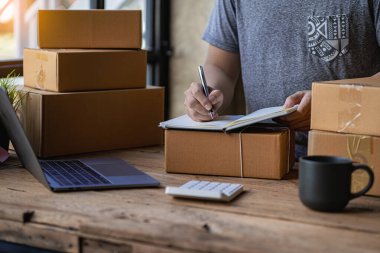 Paket kutuları ve dizüstü bilgisayarla çalışan KOBİ işletmecisi sipariş alıyor ve çevrimiçi market fikirleri taşıyordu