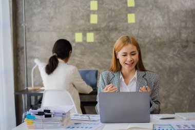 Finans konsepti ve işbirliği. Günlük giysiler içinde iki genç kadın muhasebeci dizüstü bilgisayarlar ve finansal grafik belgeleri üzerinde çalışıyor ve şirket yatırım sonuçlarını ve yıllık kazanç ve ikramiyeleri tartışıyor..