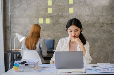 Finans konsepti ve işbirliği. Günlük giysiler içinde iki genç kadın muhasebeci dizüstü bilgisayarlar ve finansal grafik belgeleri üzerinde çalışıyor ve şirket yatırım sonuçlarını ve yıllık kazanç ve ikramiyeleri tartışıyor..