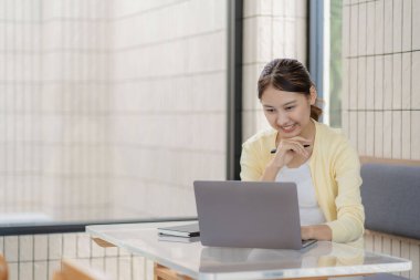 Çekici Asyalı kadın kafede bir masada tek başına oturuyor iş için dizüstü bilgisayarına bakıyor gibi görünüyor ve gülümsüyor, internette çalışıyor gibi..