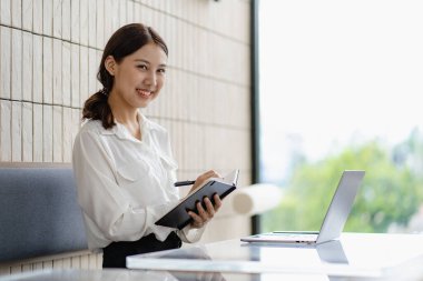 Çekici Asyalı kadın kafede bir masada tek başına oturuyor iş için dizüstü bilgisayarına bakıyor gibi görünüyor ve gülümsüyor, internette çalışıyor gibi..