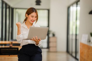 Çekici Asyalı kadın kafede bir masada tek başına oturuyor iş için dizüstü bilgisayarına bakıyor gibi görünüyor ve gülümsüyor, internette çalışıyor gibi..