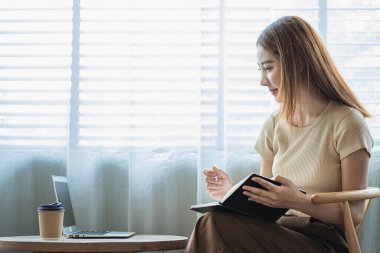 Çekici Asyalı kadın kafede bir masada tek başına oturuyor iş için dizüstü bilgisayarına bakıyor gibi görünüyor ve gülümsüyor, internette çalışıyor gibi..