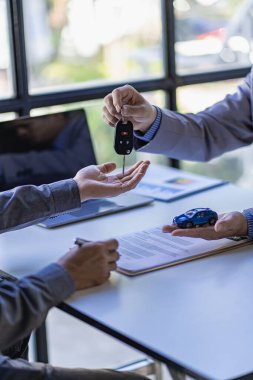 Araba kiralama konsepti. Kiralama ve satış sözleşmesini imzaladıktan sonra aracın anahtarlarını müşteriye teslim eden kişinin elleri. Yakın plan, dikey fotoğraf.