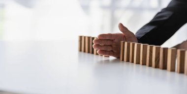 İşadamı onun el bloklamasını ya da devrilmesini durdurur. Finansal iş ve risk yönetimi. İşadamı, tahta blokların elleriyle düşmesini engeller.