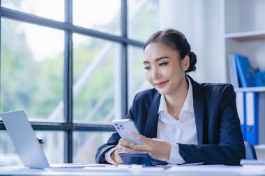 Asyalı iş kadını müşterilerle iletişim kurmak için akıllı telefon ve dizüstü bilgisayar kullanıyor, masadaki hesap makinesiyle hesaplıyor, finansal grafikleri okuyor, planlıyor, analiz ediyor, şirket ofisindeki pazar verilerini hesaplıyor..