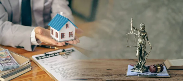 Lawyer or businessman sitting at table with fair scales Hammer and small wooden toy house work with documents Sign a contract agreement Real estate law, auction house concept