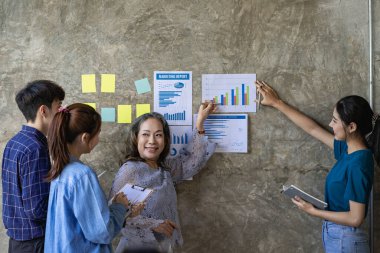 Bir grup genç iş adamı, finansal grafik ve dizüstü bilgisayarlı modern ofiste yeni bir iş kurma konusunda fikir alışverişinde bulunuyorlar.