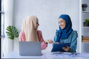 İki modern Müslüman kadın mali grafikler ve dizüstü bilgisayarla toplantı odasında iş görüşmeleri yapıyor ve tartışıyorlar.