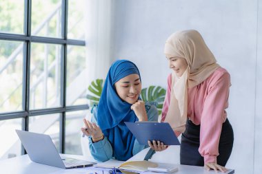 İki modern Müslüman kadın mali grafikler ve dizüstü bilgisayarla toplantı odasında iş görüşmeleri yapıyor ve tartışıyorlar.